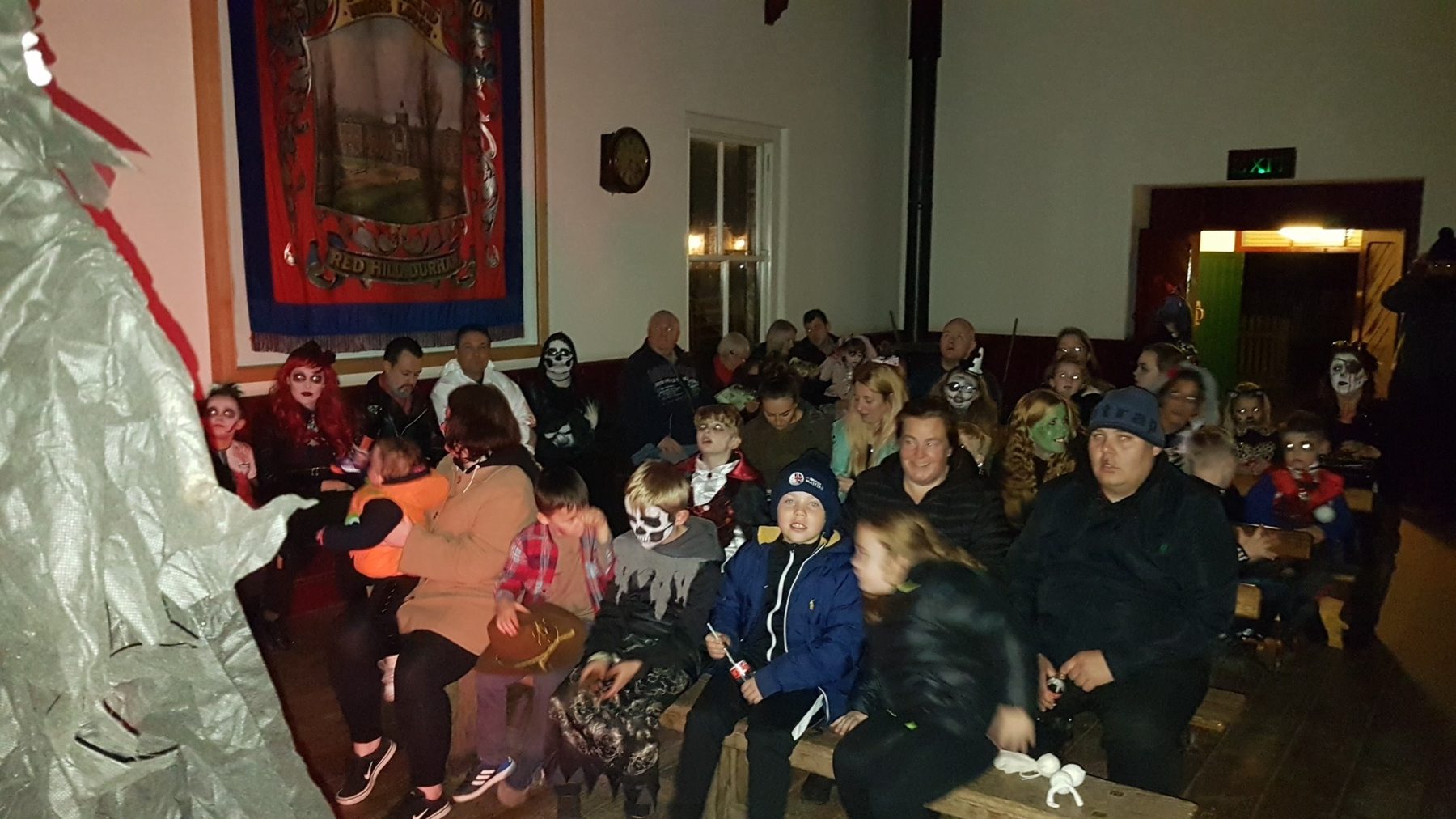 Families in Halloween costumes waiting for Professor Ron's spooky puppet show in the Band Hall at Beamish Museum