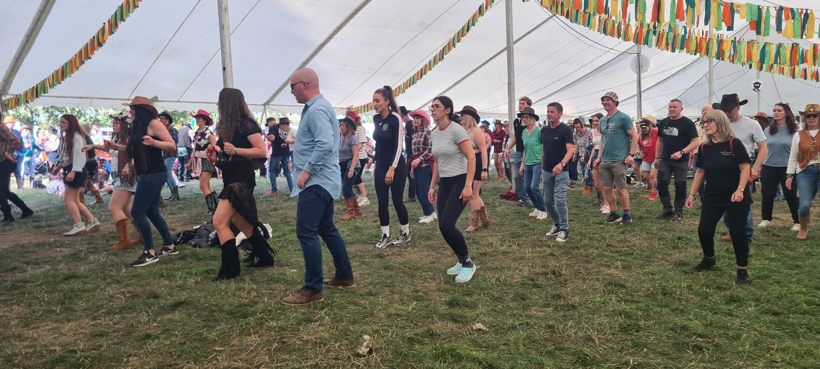 A large crowd line dancing in the marquee at Dubs int Dales