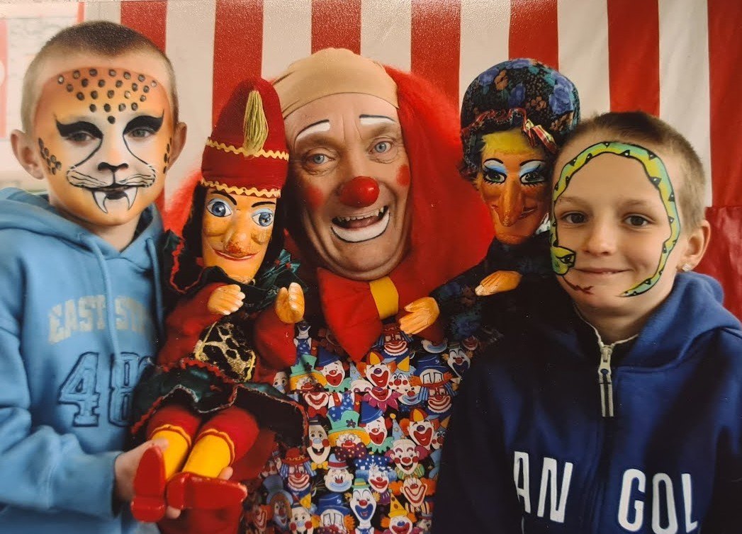 Clown with Punch and Judy puppets and two face-painted children at a family entertainment event