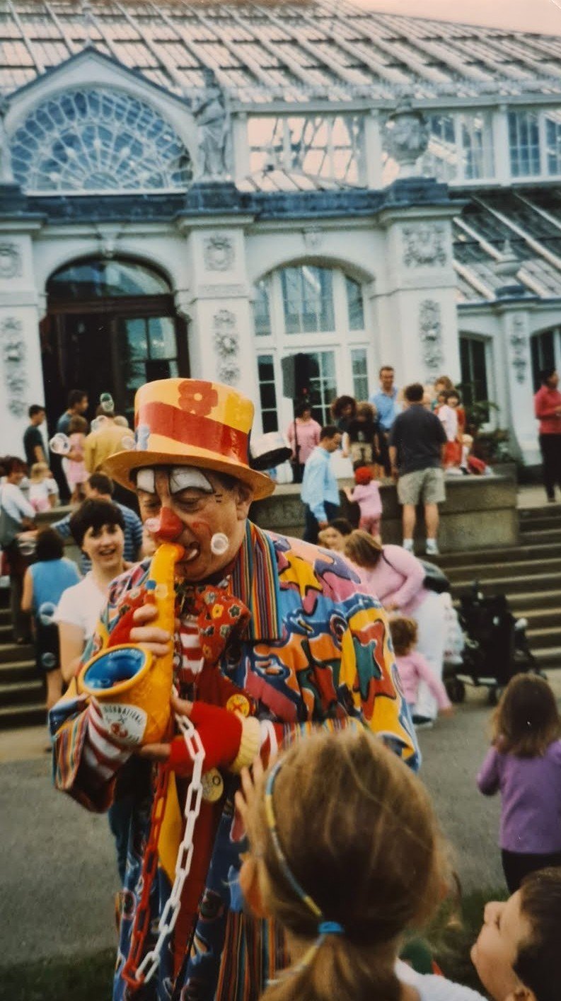 A clown entertaining children in front of the Temperate House at Kew Gardens